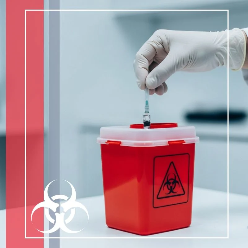 gloved hand safely disposing of a syringe into a red sharps container in a clinical setting